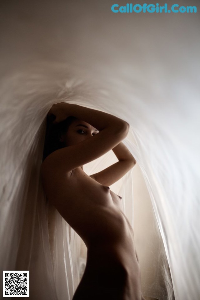 A naked woman standing in front of a white curtain.