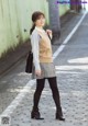 A woman in a plaid skirt and a beige sweater is posing for a picture.