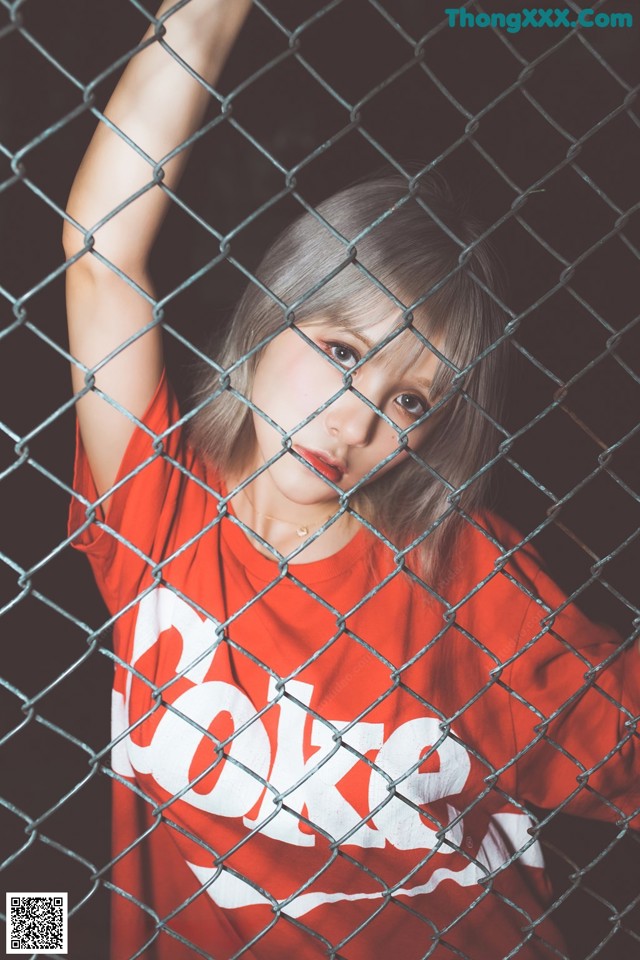 A young girl in a red shirt behind a chain link fence.