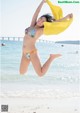 A woman in a bikini jumping in the air on the beach.