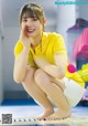 A woman in a yellow shirt and white shorts sitting on the floor.