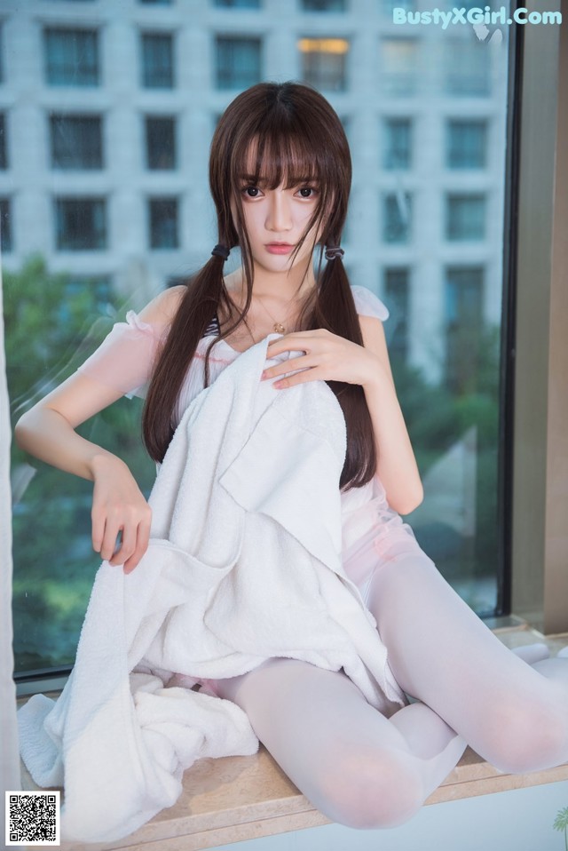 A woman sitting on a window sill wrapped in a towel.