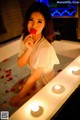 A woman in a bathtub with candles and rose petals.