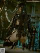 A woman in a black leather outfit is chained to a pole.