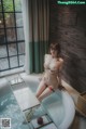 A naked woman sitting in a bathtub next to a window.